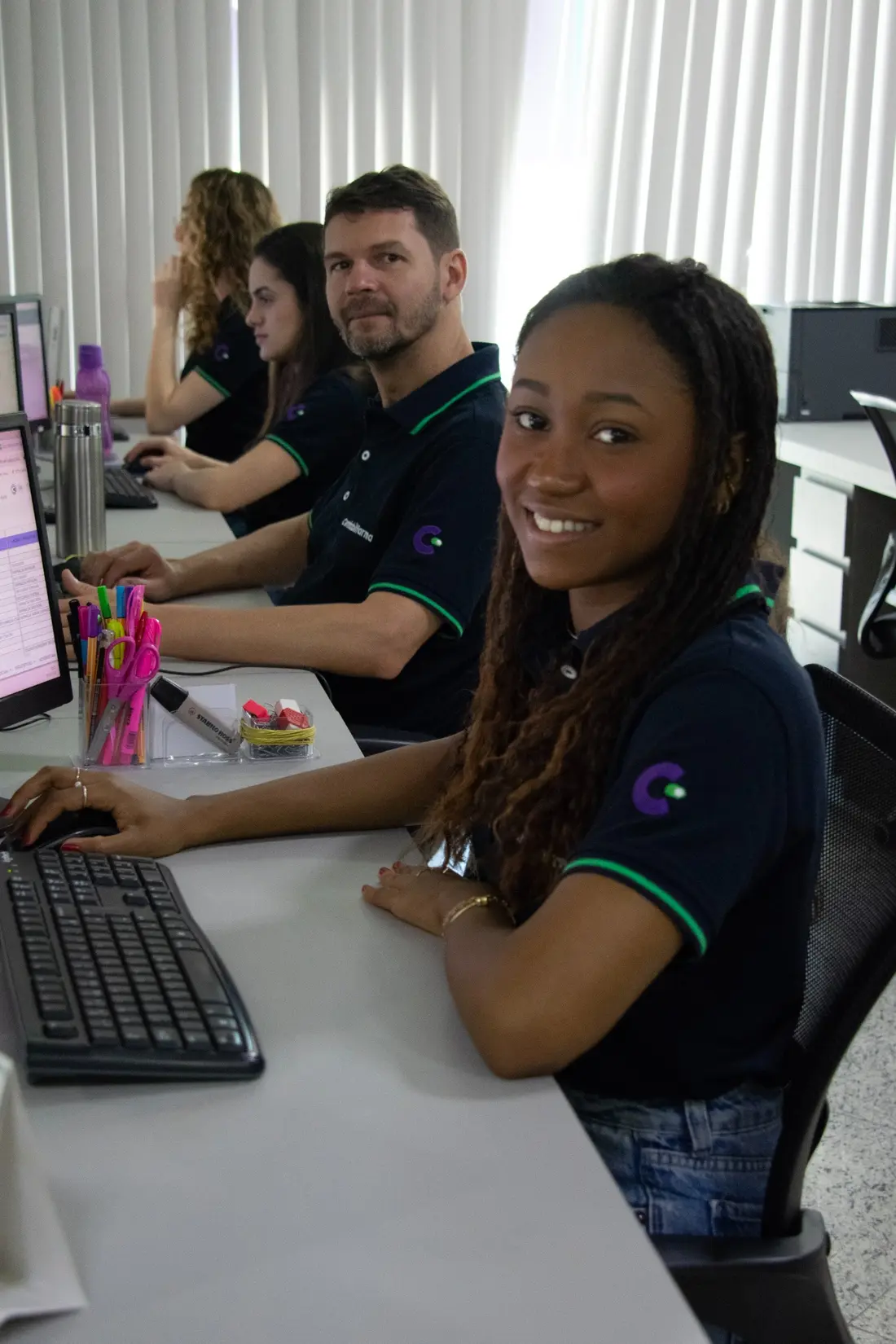Profissionais da Contabilfarma em atendimento, sorrindo para a câmera nas estações de trabalho